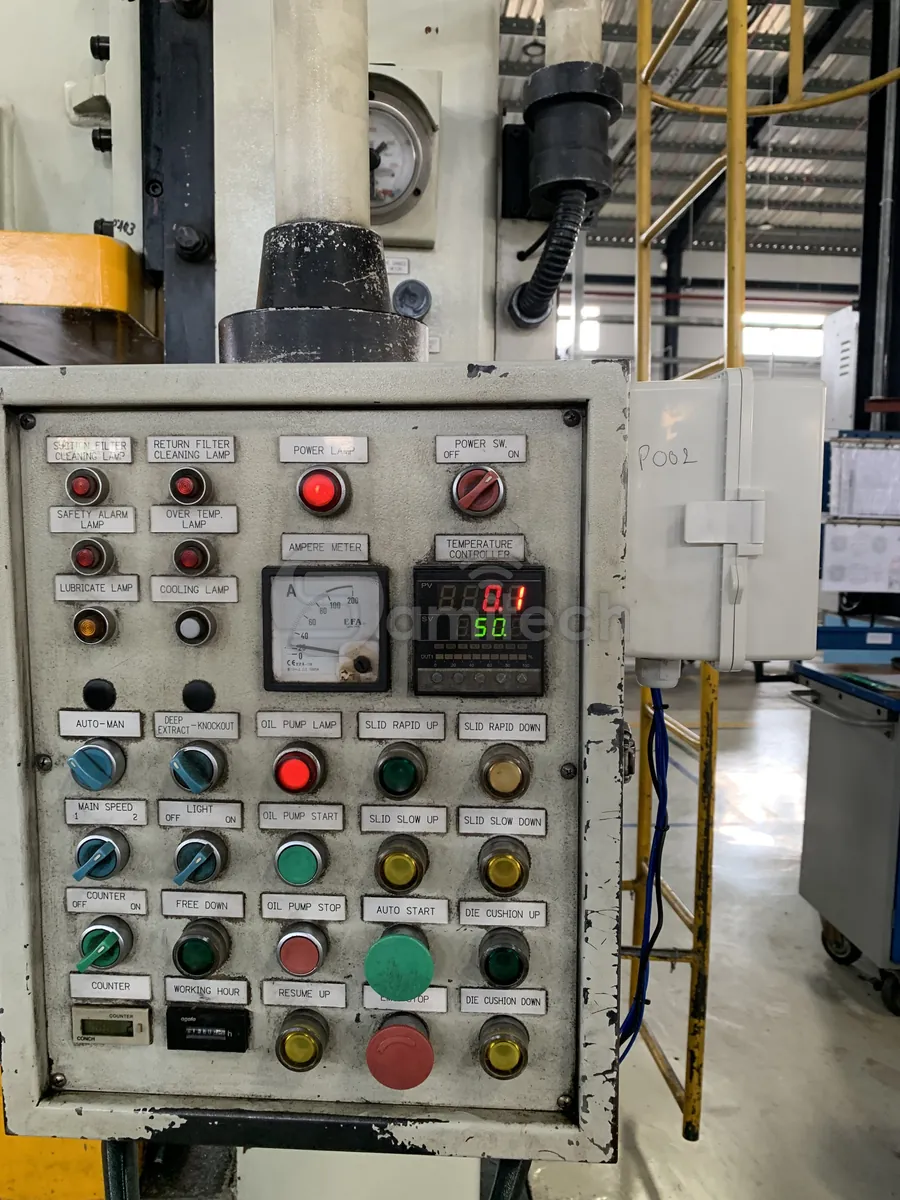 Bảng điều khiển máy dập đời cũ toàn nút bấm, đèn báo và đồng hồ kim; hộp thiết bị màu trắng treo ngay bên cạnh.