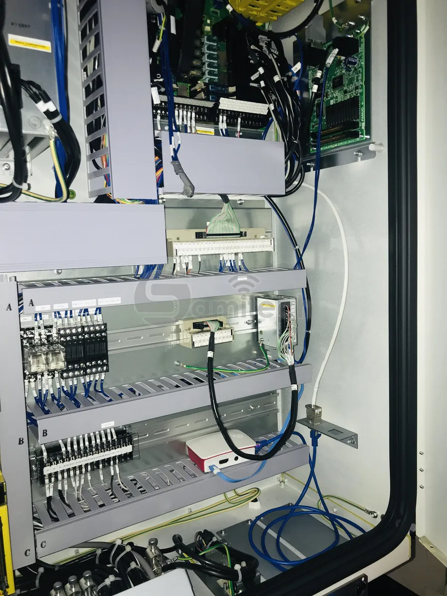 Bên trong tủ điện máy CNC: thiết bị biên nhỏ đặt trên máng cáp, nối lên bo điều khiển bằng một sợi dây LAN xanh.